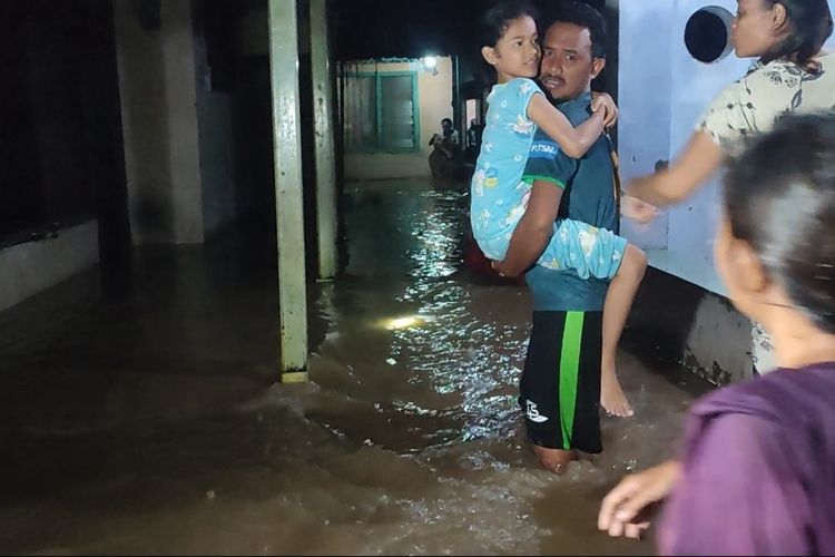 Tisna menggendong anaknya saat hujan deras dan banjir merendam rumahnya pada Kamis malam (30/3/2023). BPBD sebut ratusan rumah terendam banjir lantaran hujan deras yang mengguyur wilayah Cirebon berjam-jam.