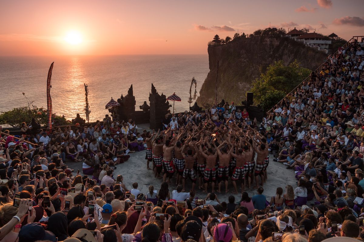 Ilustrasi tari kecak di Uluwatu, Bali, dengan latar matahari terbenam.