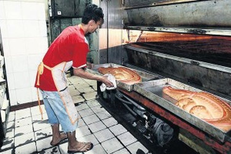 Pegawai di pabrik dan toko roti Tan Ek Tjoan, Cikini, Jakarta, mengeluarkan roti buaya pesanan pelanggan dari oven, Sabtu (8/6/2013). Roti buaya di toko ini hanya dibuat ketika ada yang memesan. Roti yang menyimbolkan kesetiaan ini selalu disertakan dalam pernikahan adat Betawi.