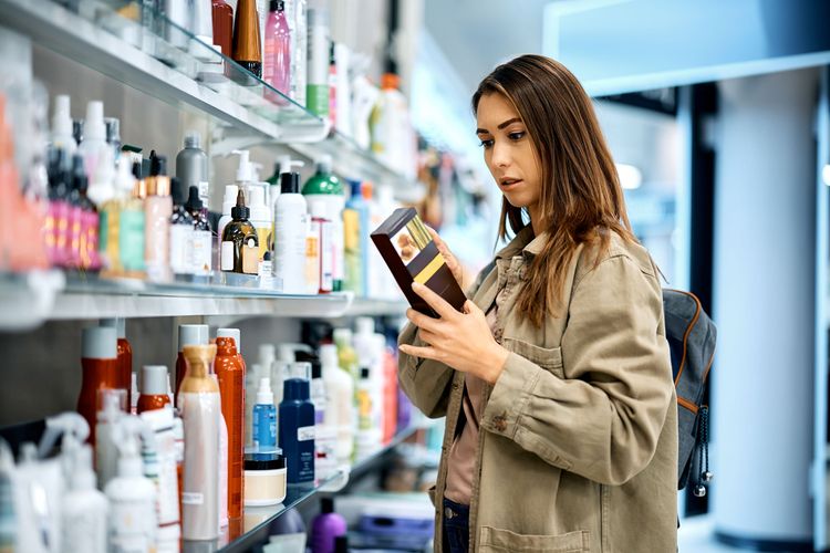 Ilustrasi seorang perempuan sedang memeriksa bahan-bahan dalam produk kosmetik.