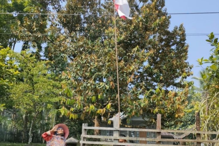 Nenek Sari Banun (74) hormat saat bendera yang dipasangnya terbalik diperbaiki Kapolsek Pangean, AKP Sony Jaselman Ritonga, di Desa Pasar Baru, Kecamatan Pangean, Kabupaten Kuantan Singingi, Riau, Rabu (10/8/2022).