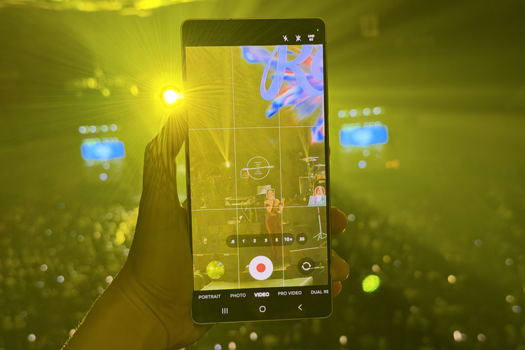 Ilustrasi merekam dan memotret panggung konser Raisa dengan di bangku penonton paling jauh