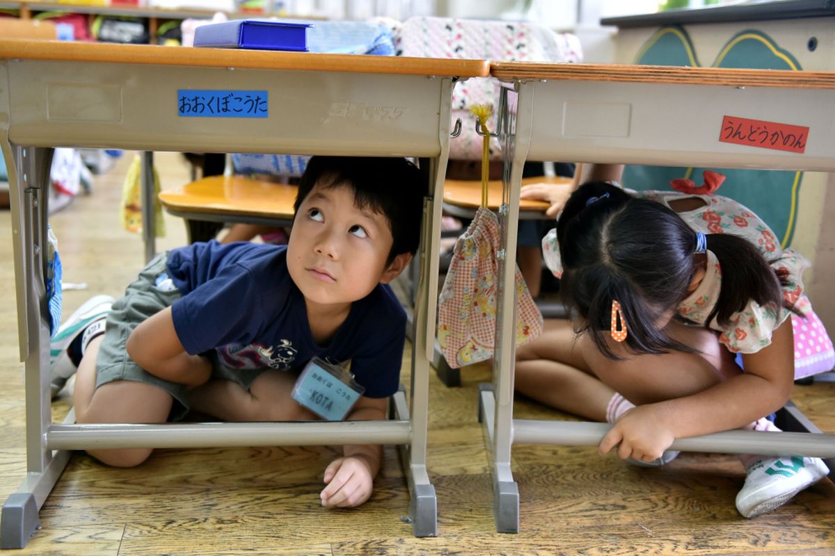Anak-anak sekolah dasar berlindung di bawah meja mereka saat latihan gempa di sebuah sekolah di Tokyo pada tanggal 1 September 2015. Latihan anti-bencana nasional diadakan pada tanggal 1 September pada hari peringatan gempa besar 1923 yang menewaskan lebih dari 100.000 orang di daerah metropolitan Tokyo.