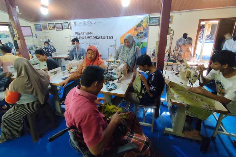 Giyarto (54) tengah membantu penyandang disabilitas lain dalam proses pelatihan yang diadakan di Sanggar Kresna Patra, di Desa Klewor, Kecamatan Kemusu, Boyolali, Sri Setyaningsih (43) pada Jumat (27/6/2025) pagi. Giyarto (di kursi roda) adalah penyandang disabilitas daksa alumni pelatihan awal. Ia dimintai bantuan oleh pendiri Kresna Patra, Sri Setyaningsih (43) untuk menyalurkan keterampilannya kepada peserta pelatihan selanjutnya.