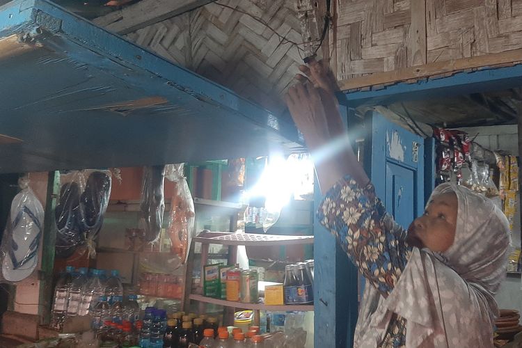 Bu Marwan (68) menyalakan lampu warungnya yang dialiri listrik hasil panel surya di atap rumahnya di Pantai Lempuyang, Dusun Merak, Taman Nasional (TN) Baluran, Desa Sumberwaru, Kecamatan Banyuputih, Kabupaten Situbondo, Minggu (18/12/2022).