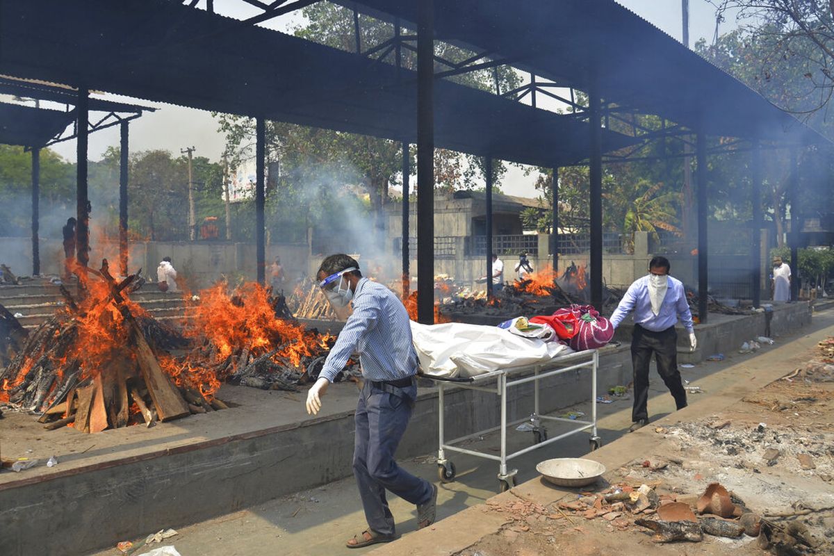 Kerabat membawa mayat seseorang yang meninggal karena COVID-19 ketika beberapa tumpukan kayu korban Covid-19 lainnya terbakar di krematorium di New Delhi, India, Sabtu (1/5/2021).