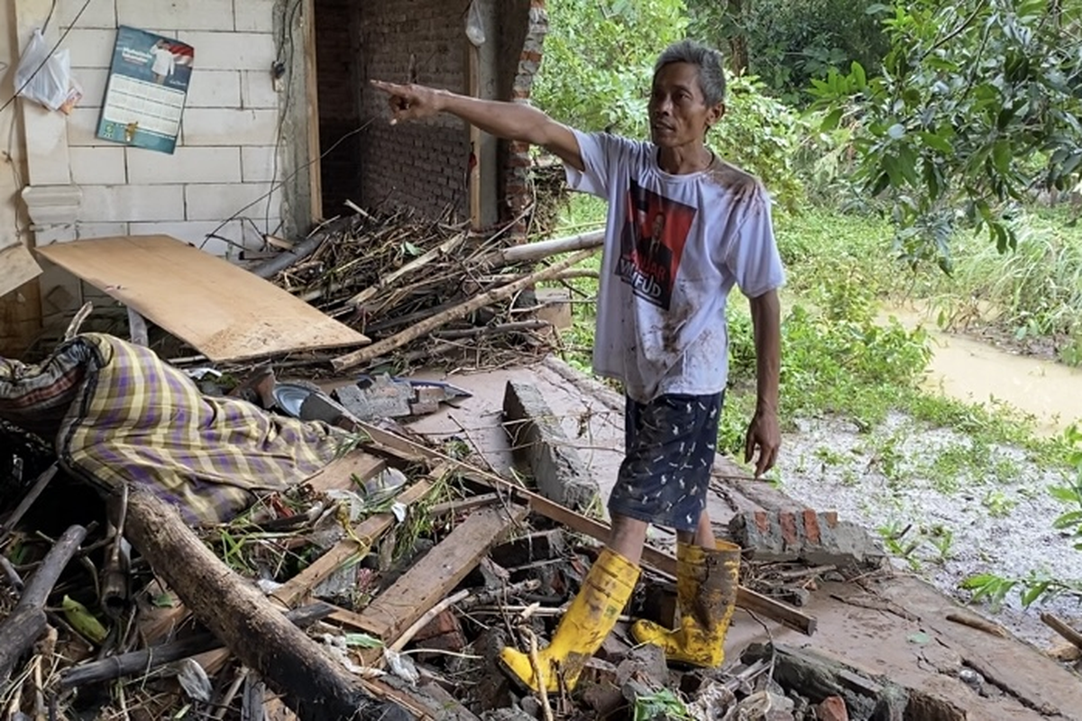 JEBOL—Darmin (60), warga Dusun Josaren, Desa Sugihwaras, Kecamatan Saradan, Kabupaten Madiun, Jawa Timur menunjukk tembok rumahnya yang jebol dihantam banjir bandang, Rabu (29/1/2025).