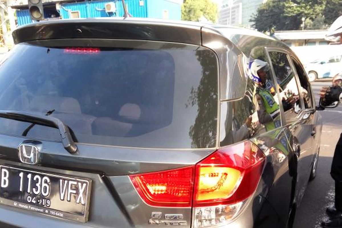 Petugas kepolisian saat menegur pengendara mobil yang berpelat nomor genap di lampu merah Bundaran Senayan pada Senin (27/6/2016). Hari ini merupakan masa uji coba penerapan ganjil genap disejumpah ruas jalan di Jakarta. 