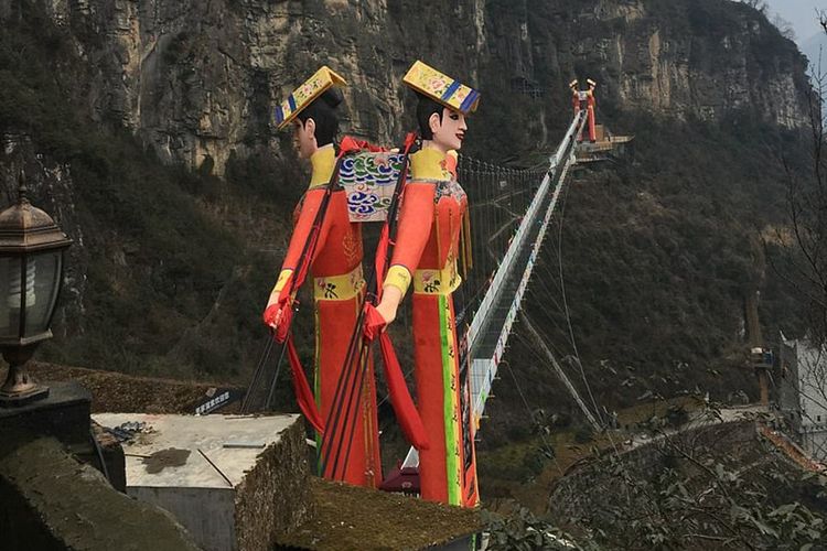 Jembatan Kaca di provinsi Sichuan yang tergantung di antara patung-patung pria dan wanita raksasa dalam kostum tradisional, yang kerap disebut patung 'selamat datang di neraka'.