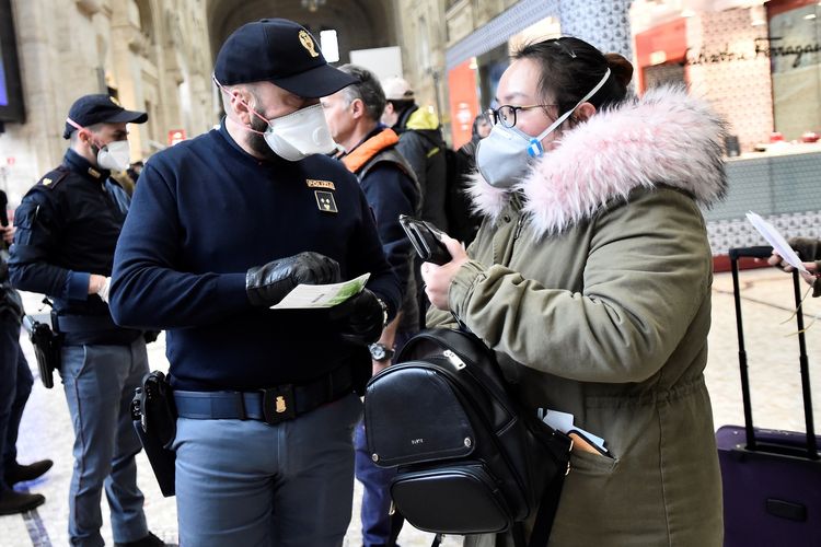 Seorang polisi yang mengenakan masker melakukan pemeriksaan terhadap calon penumpang di stasiun kereia utama di Milan, Italia, pada 9 Maret 2020. Pemerintah Italia menerapkan karantina buntut virus corona yang merebak.