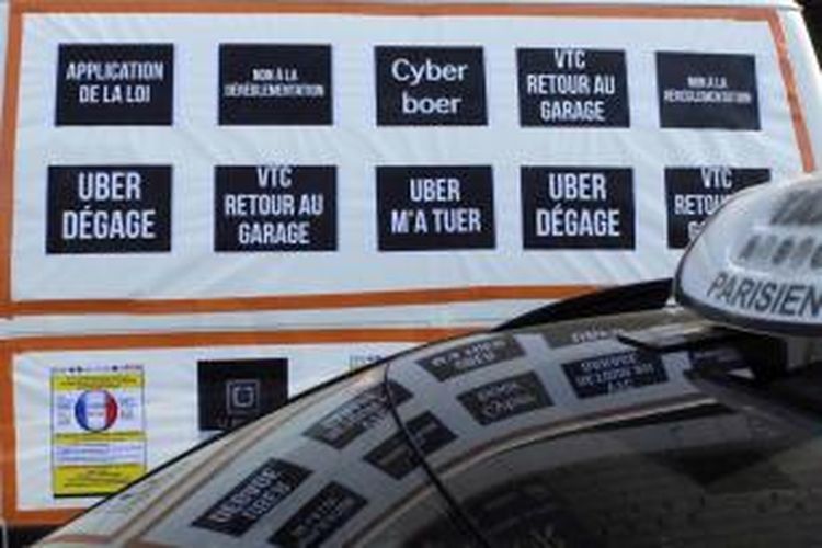 Sebuah van dengan poster bertuliskan slogan-slogan memprotes jasa layanan sewa mobil Uber, dalam aksi demonstrasi di Paris, 25 Juni 2015. Para sopir taksi memblokir jalan menuju Bandara Charles de Gaulle, hingga membuat macet.