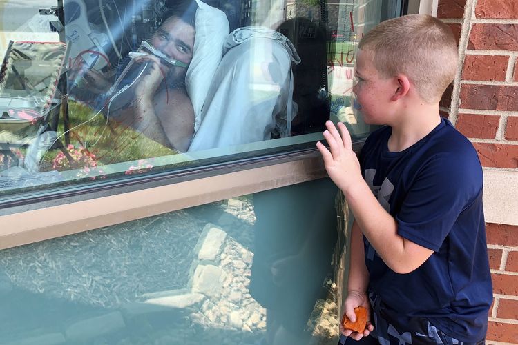 Brody Barker (6) melambaikan tangan kepada ayahnya, Daryl, dari luar kamar rumah sakit pada Senin (26/7/2021) di Osage Beach, Missouri, Amerika Serikat. Brody dan ibunya, Billie, sudah hampir tiga minggu menanti di luar ICU Lake Regional Hospital menunggu Daryl pulih dari Covid-19.