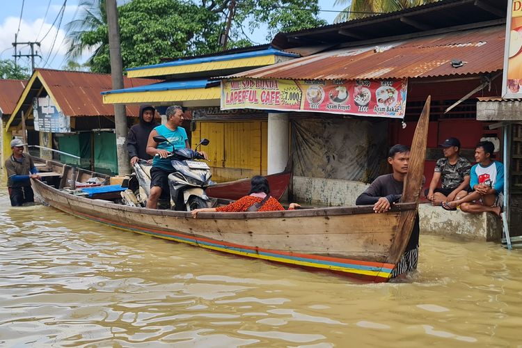 Situasi Wan (50) sedang mengevakuasi sepeda motornya pakai sampan di Jalan Khairil Anwar, Kelurahan Tanjung Pura, Kabupaten Langkat, pada Rabu (3/12/2025). 