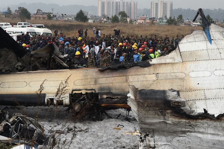 Petugas penyelamatan Nepal berada di sekitar puing-puing sebuah pesawat terbang yang jatuh di dekat bandara internasional di Kathmandu, Senin (12/3/2018). (AFP/Prakash Mathema)