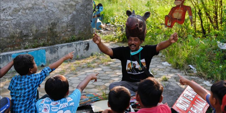 Samsudin mengenakan topi berbentuk kuda nil memainkan boneka-boneka tentang hewan-hewan endemik di Indonesia saat mendongeng untuk anak-anak di Indramayu, Jawa Barat, 12 Maret 2021