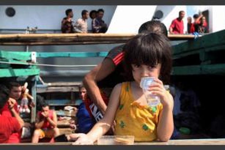 Seorang bocah bersama orang tua para pencari suaka asal Iran di atas perahu saat berada di Pelabuhan Benoa, Bali, usai ditangkap polisi di perairan Selat Badung, Minggu (12/5/2013). Para imigran gelap yang berjumlah 100 orang itu diperkirakan akan menuju Australia.