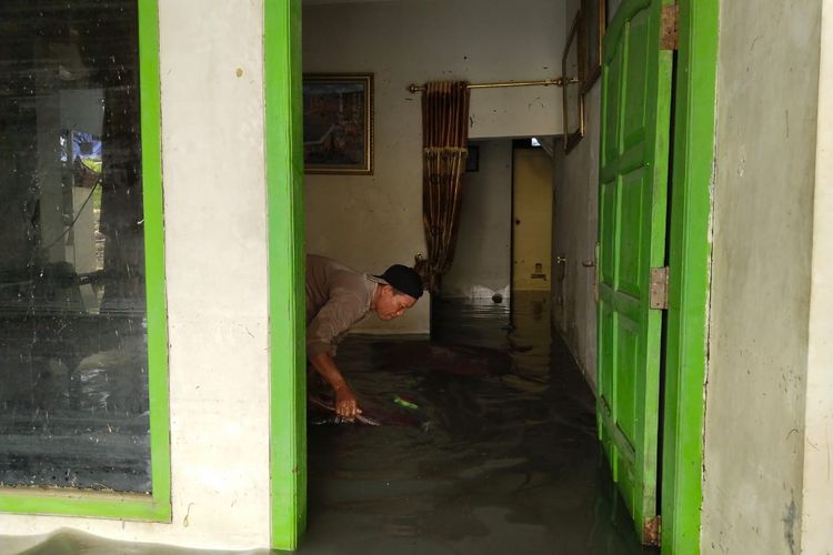 Salah seorang warga Desa Karanganyar, Kecamatan Karanganyar membersihkan lumpur di lantai yang masih tergenang air, Jumat (16/2/2024). 