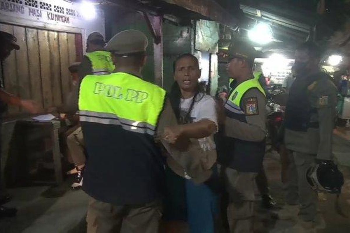 Seorang wanita pemilik warung kelontong yang menjual minuman keras di Kelapa Gading marah-marah saat dirazia petugas Satpol PP Jakarta Utara, Senin (13/3/2023) malam kemarin. 
