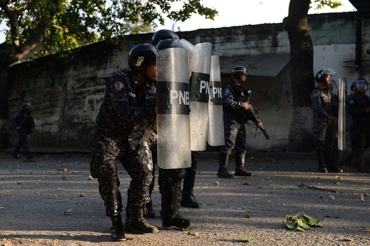 Polisi antihuru-hara berlindung dari lemparan batu dari demonstran dalam aksi unjuk rasa anti-pemerintah di Caracas, pada Senin (21/1/2019).