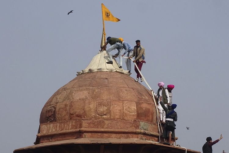 Sikh mengibarkan Nishan Sahib, bendera agama Sikh, di menara monumen bersejarah Benteng Merah di New Delhi, India, Selasa, 26 Januari 2021. Puluhan ribu petani yang memprotes mengendarai traktor panjang ke ibu kota India pada hari Selasa , menerobos barikade polisi, melawan gas air mata, dan menyerbu Benteng Merah yang bersejarah saat negara itu merayakan Hari Republik.