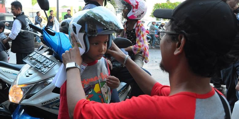 Kutu Community membagikan helm gratis untuk anak-anak di jalan raya.