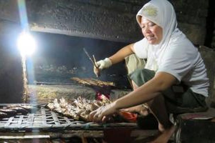 Purwati (36) memanggang atau mengasapi ikan mujair di dalam tungku berbahan bakar batok kelapa di rumahnya, Desa Penatarsewu, Kecamatan Tanggulangin, Sidoarjo, Jawa Timur, Rabu (11/11/2015). Setiap hari, ibu dua anak ini bekerja sejak pukul 09.00 hingga 17.00, memanggang 150 kilogram ikan. Ikan segar dibeli seharga Rp 23.000 per kg, dan dijual dalam bentuk ikan asap seharga Rp 50.000 per kg.