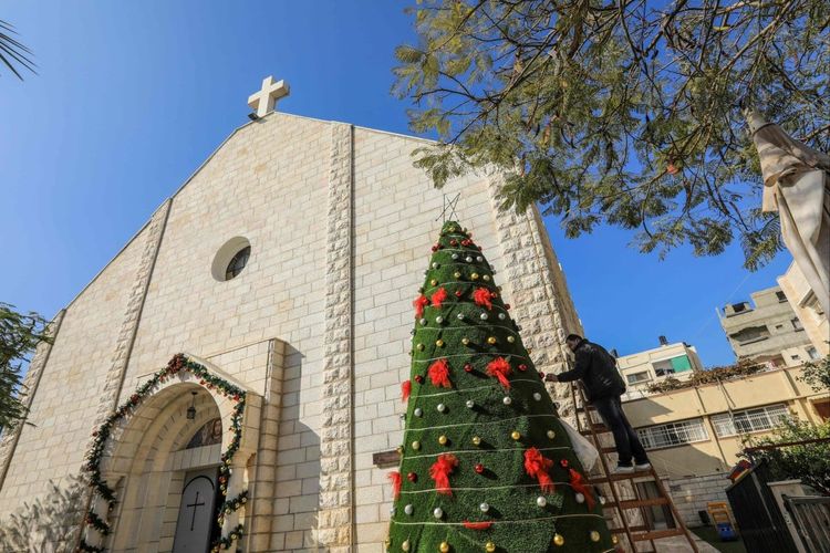 Seorang pria mendekorasi pohon Natal di luar Gereja Keluarga Kudus Katolik Roma di Kota Gaza pada Desember 2020. Pada Sabtu (16/12/2023), tentara Israel disebut telah menembak mati dua perempuan di halaman gereja yang tengah digunakan sebagai tempat berlindung tersebut.