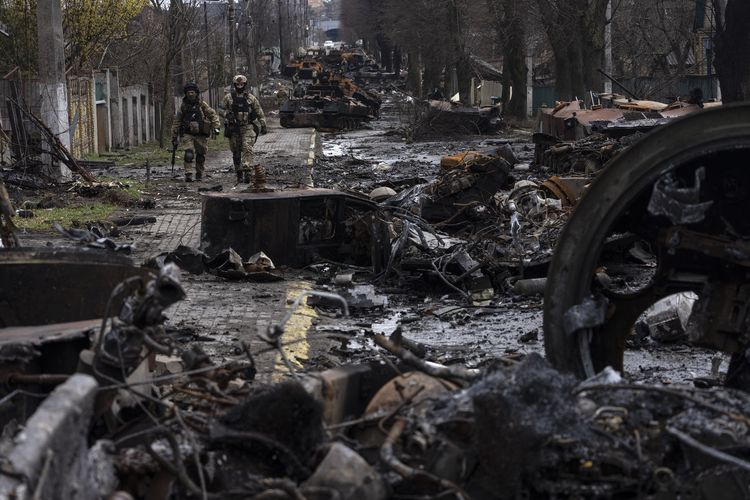 Dua tentara berjalan di sekeliling tank-tank Rusia yang hancur di Bucha, pinggiran Kyiv, Ukraina, Minggu (3/4/2022). Tentara Ukraina menemukan jasad-jasad manusia yang tewas secara brutal dan kerusakan massal di pinggiran Kyiv, lalu meminta penyelidikan kejahatan perang dan sanksi baru terhadap Rusia.