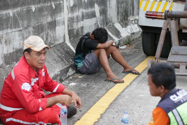 Sopir truk kontainer bermuatan cat yang terguling di pintu keluar tol Cijago di Jalan Juanda, Depok, tertunduk lesu usai kecelakaan, Kamis (10/11/2022). Kecelakaan tunggal itu dipastikan tak ada korban jiwa maupun luka-luka.