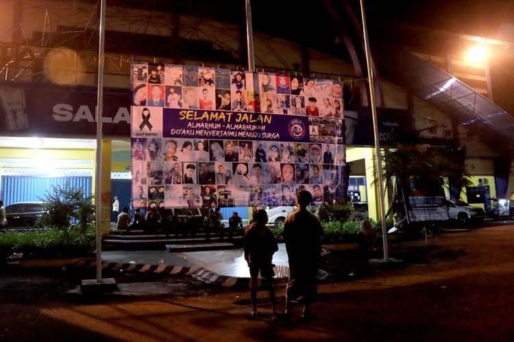 Dua orang peserta doa bersama Aremania sedang melihat foto-foto korban meninggal tragedi saat mengenang 100 hari Tragadi Kanjuruhan yang digelar depan pintu utama Stadion Kanjuruhan Kepanjen, Kabupaten Malang, Senin (9/1/2023) malam.