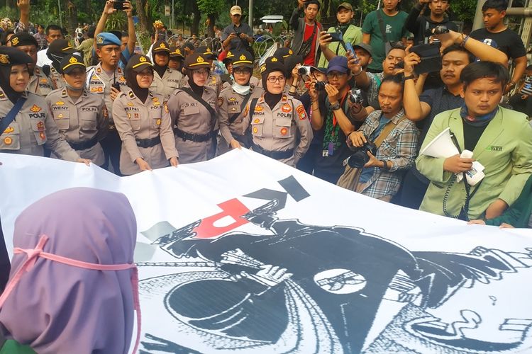 Barisan Polisi Wanita (Polwan) menerima spanduk berukuran besar yang disodorkan mahasiswi peserta aksi unjuk rasa di sekitar Patung Kuda, Jalan Medan Merdeka Barat, Jakarta Pusat, Kamis (17/10/2019). Spanduk itu bergambar tikus berdasi yang tengah menggondol pundi-pundi sembari menginjak logo KPK.