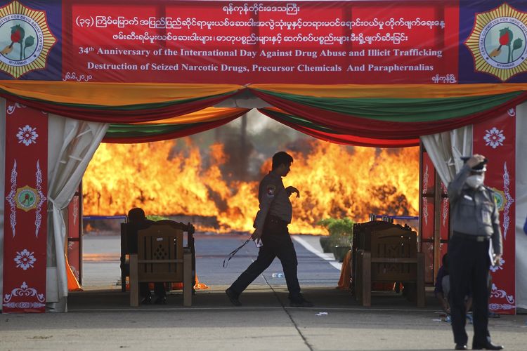 Polisi berdiri di sekeliling narkoba yang dibakar dalam acara upacara penghancuran bukti kejahatan di Yangon, Myanmar, pada 26 Juni 2021. Militer Myanmar menyatakan mereka menghancurkan barang bukti narkotika sekitar 500 juta poundsterling, atau Rp 10triliun.