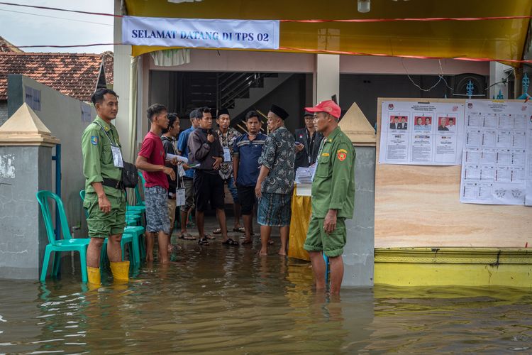 Petugas ketertiban Tempat Pemungutan Suara (TPS) menjaga area TPS 02 yang terkepung banjir di Desa Ngelowetan , Kecamatan Mijen, Kabupaten Demak, Jawa Tengah, Rabu (14/2/2024). Sejumlah TPS di Kecamatan Mijen terpaksa dipindahkan ke area yang lebih aman dari genangan  banjir pada hari Pemilu 2024 karena adanya banjir di luar prediksi pada Selasa (13/2) dini hari limpasan aliran banjir Kecamatan Karanganyar, Kabupaten Demak.