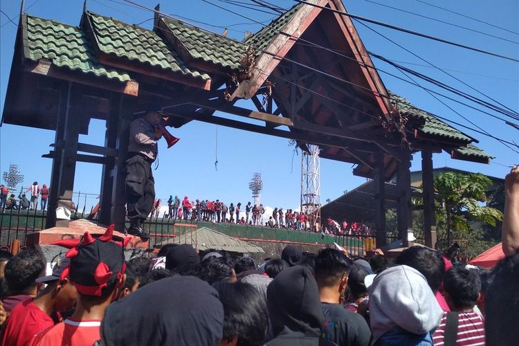 Seorang polisi harus berdiri di atas pintu masuk stadion Andi Mattalatta untuk menenangkan suporter yang mulai saling dorong, Selasa (6/8/2019).