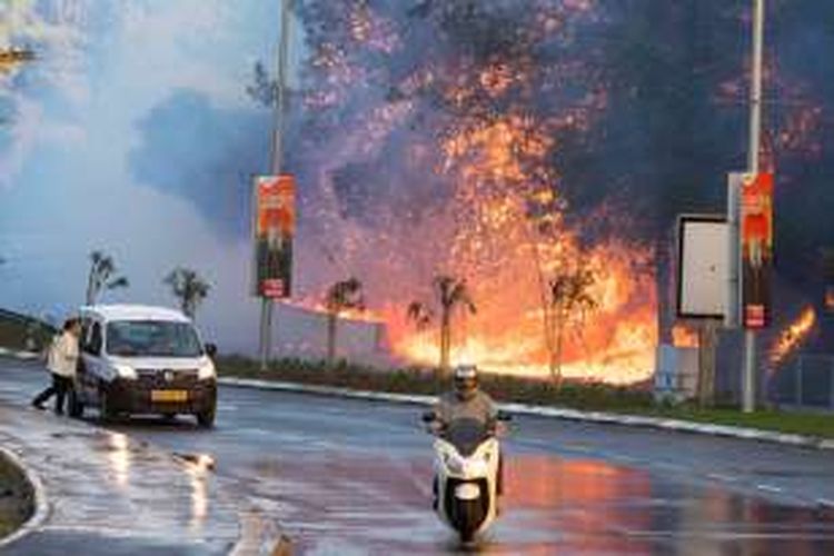 Pengguna jalan di kota Haifa melintas di dekat kobaran api yang cukup besar yang diakibatkan kebakaran lahan yang terjadi selama tiga hari terakhir.