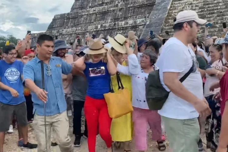 Tangkap layar massa yang marah melempari seorang turis wanita dengan air dan memakinya setelah dia menaiki tangga dan joget-joget setelah mencapai puncak kuil piramida Maya kuno di semenanjung Yucatan Meksiko.

