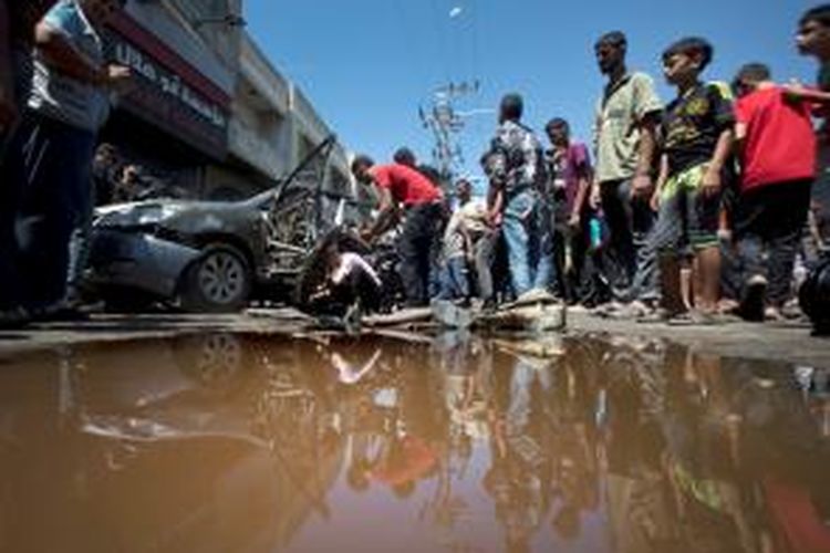 Warga Gaza City berkumpul di sekitar sebuah mobil yang menjadi sasaran tembakan roket jet tempur Israel, Selasa (8/7/2014). Serangan udara Israel di Gaza mengakibatkan 13 orang tewas dan 90 orang lainnya terluka.