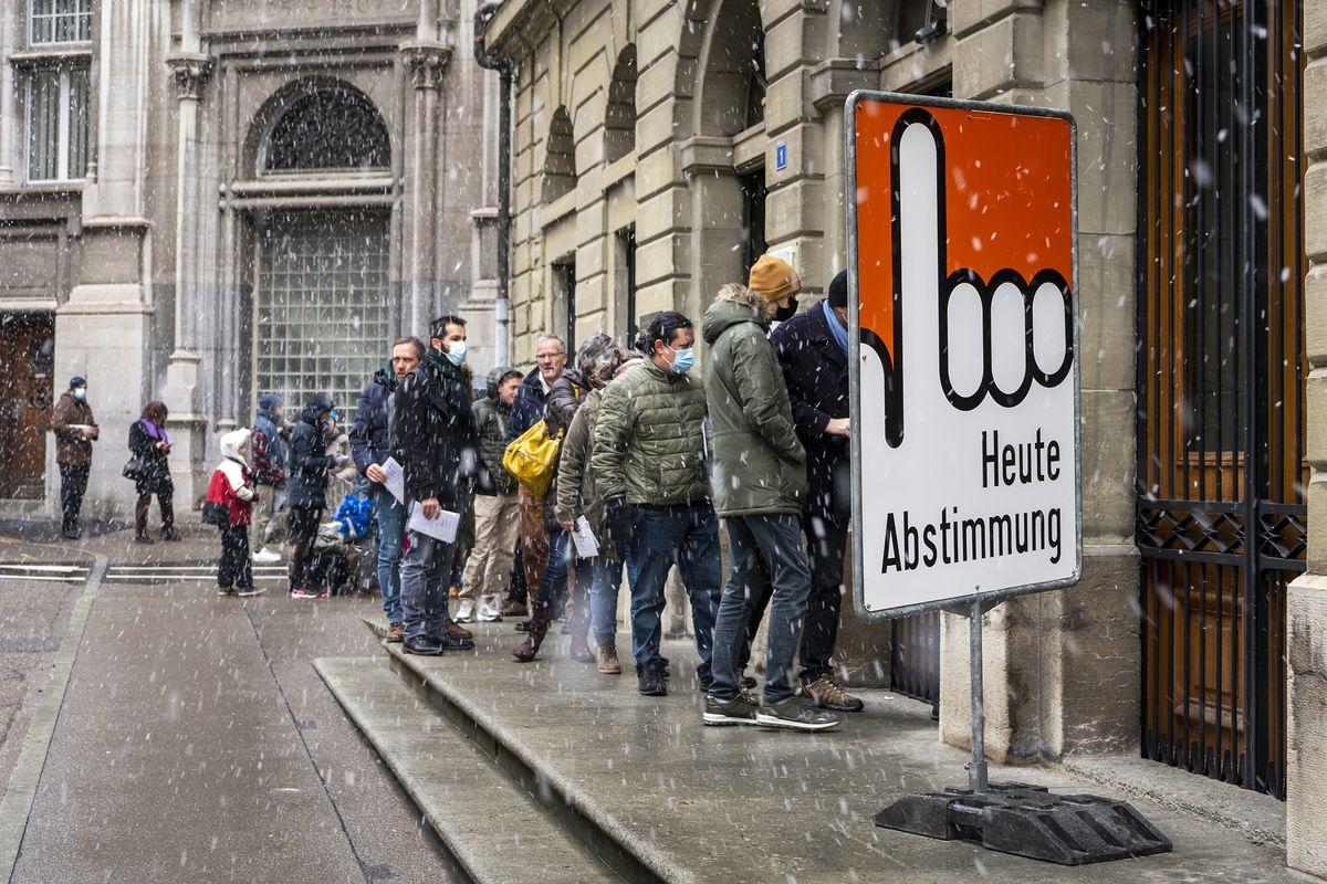 Antrean rakyat Swiss di bawah guyuran salju saat memberikan suara untuk referendum Covid-19 di Fribourg, Minggu (28/11/2021). Mayoritas rakyat Swiss menyetujui penggunaan Covid Pass, sertifikat yang menunjukkan seseorang sudah divaksin atau sembuh dari Covid-19, sebagai syarat masuk acara publik atau perkumpulan.