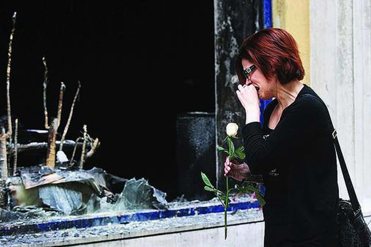 Seorang wanita menangis dan meletakkan karangan bunga di sebuah cabang Bank Marfin, Kamis (6/5) di Athena, Yunani. Sehari sebelumnya, tiga orang tewas di lokasi bank ini akibat lemparan bom molotov. Aksi protes massa Yunani semakin berkembang liar menjadi aksi kerusuhan.