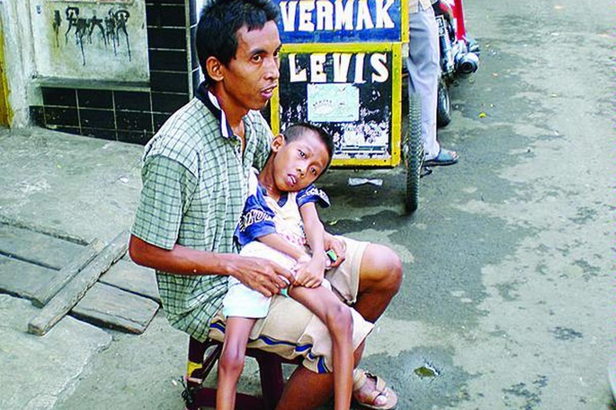 Amri (10) dalam pangkuan bapaknya, Aang (30), terkulai dengan kondisi yang memprihatinkan. Badan kurus kering, tak bisa berbicara, hanya rintihan dan air mata. Setiap hari, di kawasan Pasar Tanah Abang, orangtua Amri berharap ada orang yang mau membantu untuk memenuhi kebutuhan makan dan obat.  