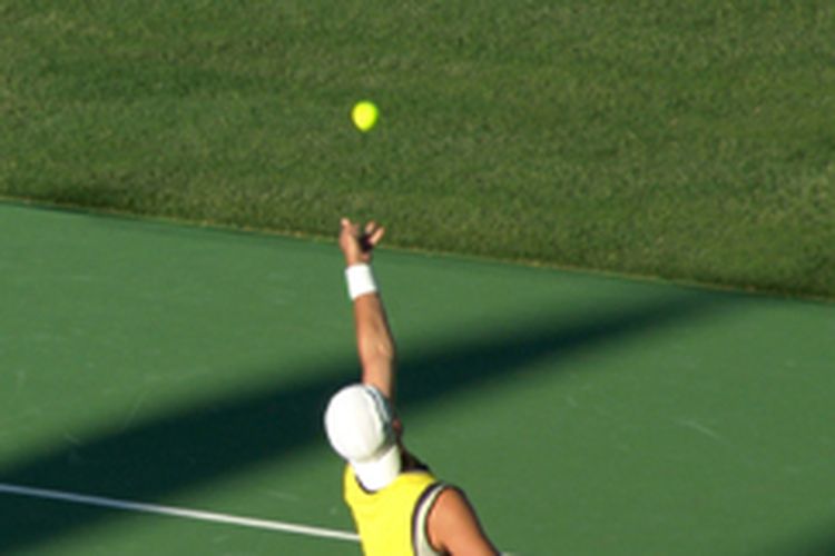 Seorang atlet tenis profesional sedang menservis bola.
