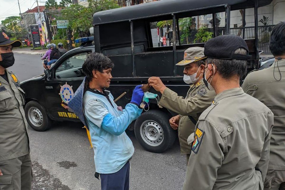 Petugas Satpol PP Kota Denpasar saat memberikan masker medis kepada Nengah Budiasa setalah sebelumnya menggunakan masker yang terbuat dari batok kelapa  