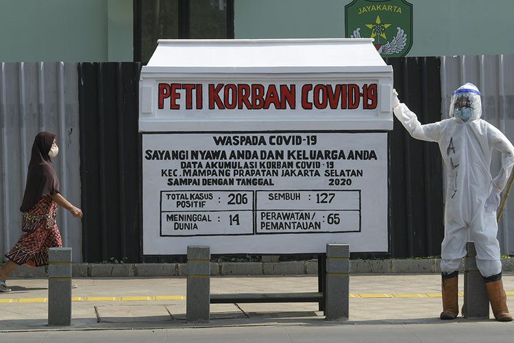 Warga melintas di samping replika peti mati dengan petugas yang menggunakan APD di kawasan Kemang, Jakarta, Minggu (16/8/2020). Kegiatan tersebut untuk menyosialisasikan bahaya Covid-19 yang dapat menyebabkan kematian.