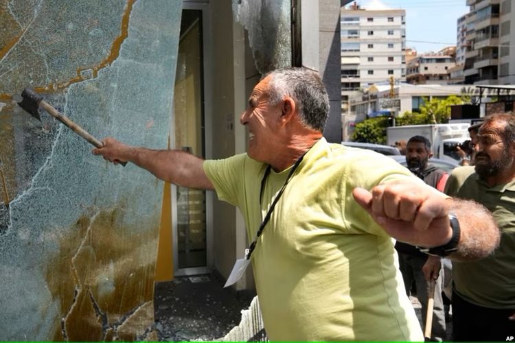 Seorang nasabah yang marah memecahkan jendela di cabang Bank Byblos selama aksi protes menuntut pencairan dana tabungan para deposan, di Beirut, Lebanon, Kamis, 15 Juni 2023. 