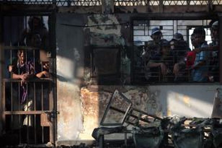 Narapidana berada di balik jeruji tahanan dengan bangunan yang terbakar di Lembaga Pemasyarakatan (Lapas) Klas I Tanjung Gusta, Medan, 12 Juli 2013.  Lapas dibakar narapidana pada 11 Juli. Dua petugas dan tiga narapidana tewas serta 150 narapidana kabur, termasuk narapidana teroris.