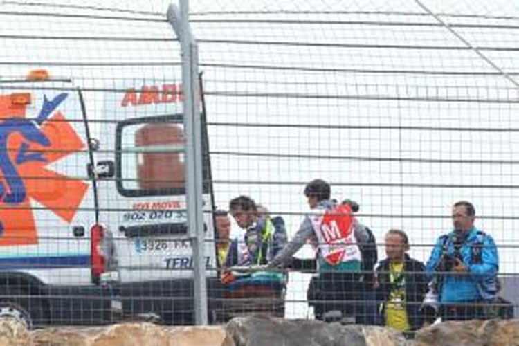 Pebalap Movistar Yamaha asal Italia, Valentino Rossi, masuk mobil ambulan dengan bantuan para marshal setelah terjatuh pada lap keempat balapan GP Aragon di Sirkuit Motorland Aragon, Minggu (28/9/2014).