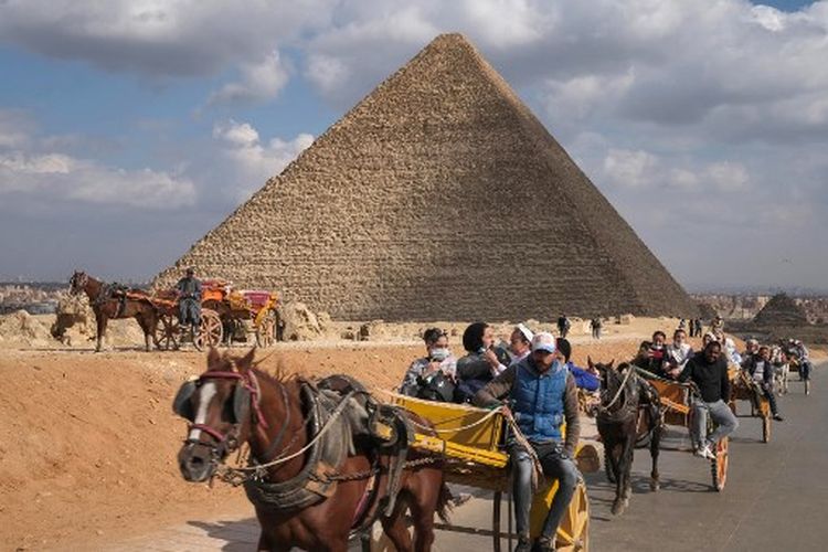 Orang-orang menaiki kereta melewati piramida Khufu (Cheops) di pekuburan piramida Giza di pinggiran barat daya ibu kota Mesir, Kairo, pada 17 Desember 2021.
