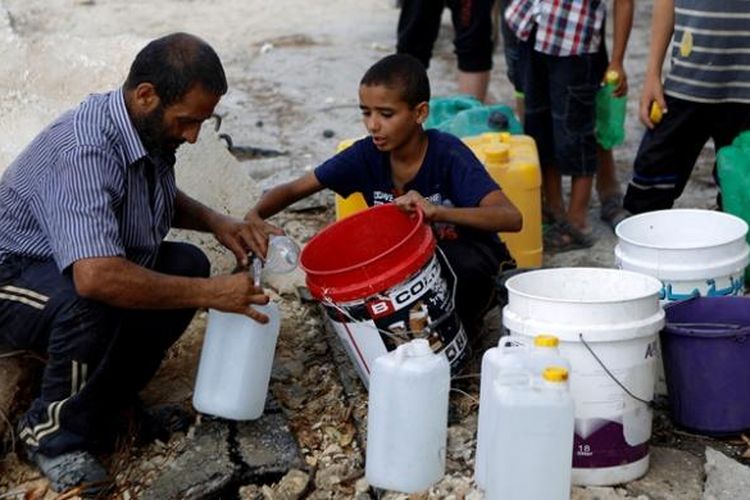Seorang pria dan sejumlah anak-anak mengisi wadah-wadah plastik dengan air di wilayah Al-Shejaea, Jalur Gaza di tengah gencatan senjata selama 72 jam, setelah konflik bersenjata selama sebulan yang menewaskan lebih dari 1.800 warga Gaza.