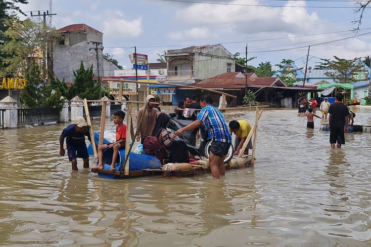 Situasi Wan (50) sedang mengevakuasi sepeda motornya pakai sampan di Jalan Khairil Anwar, Kelurahan Tanjung Pura, Kabupaten Langkat, pada Rabu (3/12/2025). 