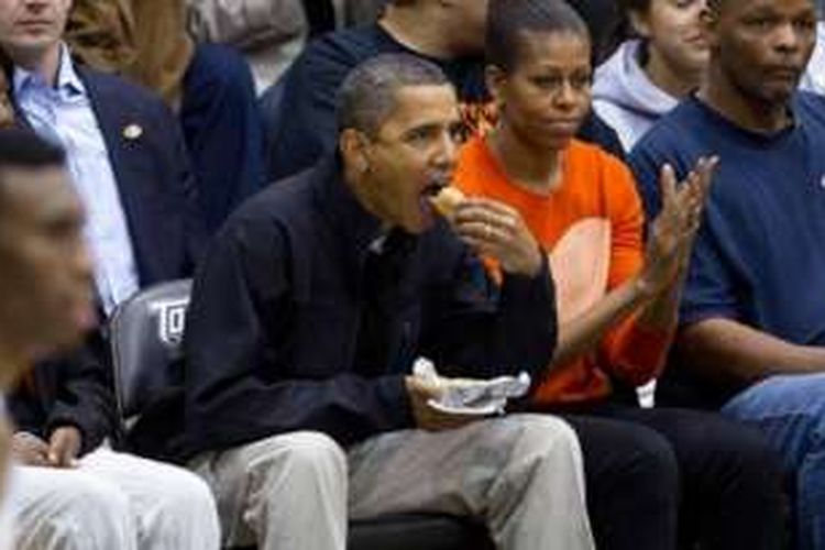 Presiden AS Barack Obama menyantap hotdog sambil menyaksikan pertandingan basket bersama ibu negara Michelle Obama.